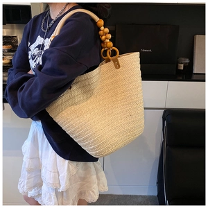 Detail of hand-woven straw tote bag featuring decorative wooden bead handles and rings