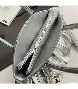 Detail view of silver ruched handbag showing smooth zipper closure and pearl chain