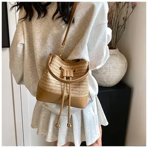 Detail of woven straw bucket bag with brown leather trim and adjustable shoulder strap