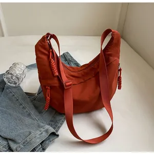 Close-up of rust orange crescent canvas bag featuring woven rope zipper and adjustable strap