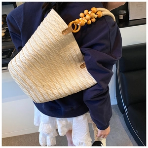 Detail of hand-woven straw shoulder bag featuring decorative light wood bead straps