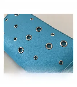 Detail of bright blue litchi grain leather bag with decorative silver metal grommets