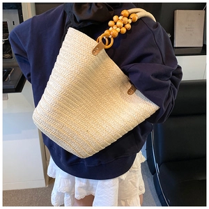 Detail of straw tote bag featuring large wooden bead handle and spacious woven texture