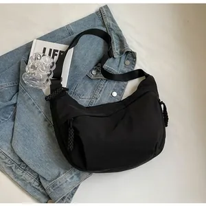 Detail of black crescent crossbody bag with braided rope zipper pull on denim background