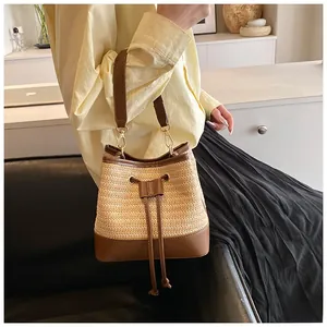 Detail of woven straw bucket bag with dark brown leather trim and drawstring closure