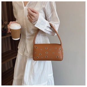 Detail of brown leather underarm bag featuring decorative silver metal eyelets and sleek handle