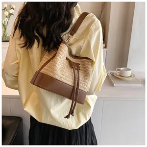 Detail showing woven straw bucket bag with dark brown leather straps and drawstring