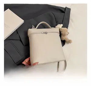 Detail of off-white lychee texture leather backpack with a cute brown plush bear charm