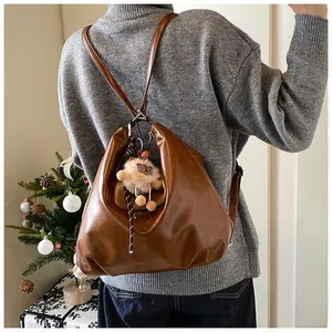 Brown soft leather backpack with cute plush bear pendant shown in a cozy home setting