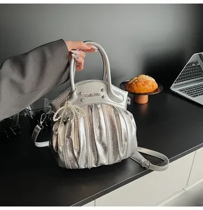 Detailed close-up of a silver pleated handbag with pearl bow charm and metal logo