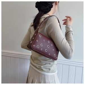 Detail of dark burgundy underarm bag with silver metal eyelets on lychee texture leather