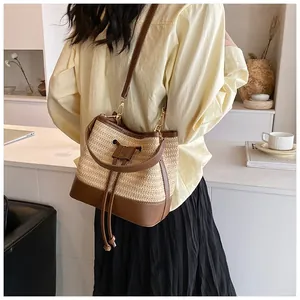 Detail of straw woven bucket bag with leather strap worn by a woman on a bright background