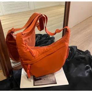 Detail of vibrant orange nylon hobo bag showing adjustable strap and woven zipper puller