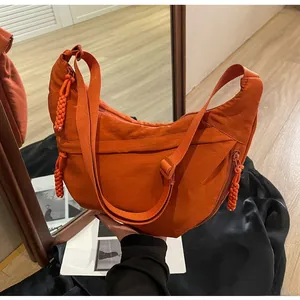 Detail of orange nylon dumpling bag featuring woven zipper pull and adjustable strap