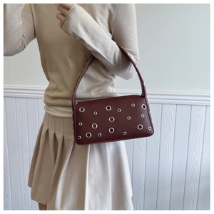 Detail of burgundy faux leather underarm bag with silver eyelets and smooth zipper closure