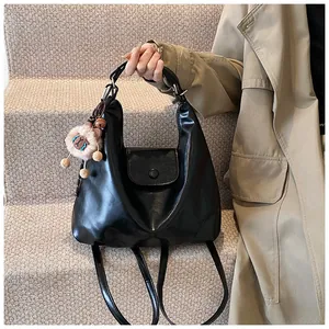 Detail of a matte black Hobo backpack with a brown plush lion charm on beige stairs