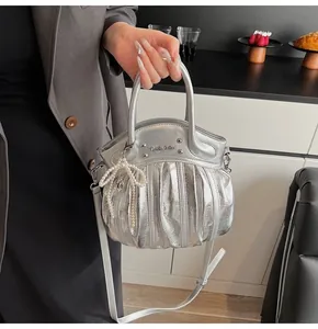 Close-up of silver ruched handbag with pearl bow charm and metallic brand logo detail