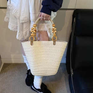 Minimalist straw tote bag with beaded wooden handle shown with model in white dress