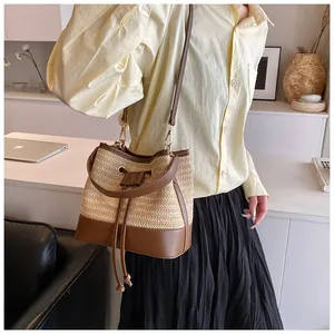 Detail of hand-woven straw bucket bag with dark brown leather trim and golden hardware