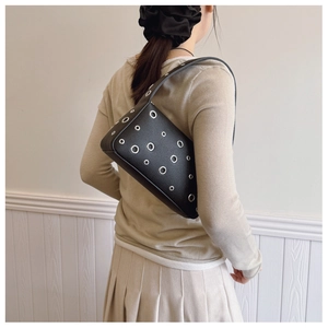 Detail of black faux leather underarm bag with silver metal eyelets and shoulder strap