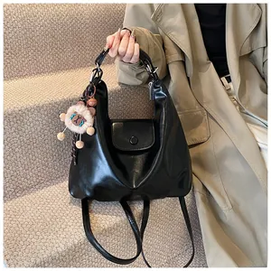 Detail of a matte black leather handbag with a plush animal charm on the handle