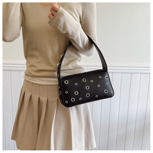Detailed view of black leather underarm bag with decorative silver metal eyelets for women