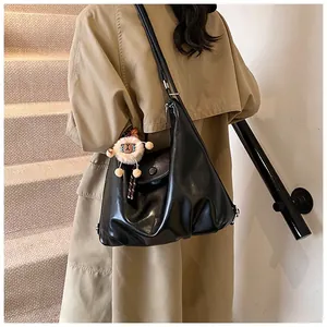 Chic black polished leather crossbody bag shown on a model with a cute plush pendant