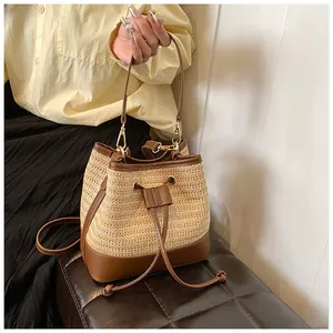 Detail of hand-woven straw bucket bag with brown leather trim and golden metal hardware