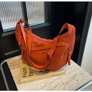 Close-up of orange dumpling bag with woven zipper detail and adjustable strap