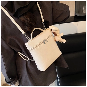 Detail of off-white lychee grain backpack featuring a cute plush dog pendant accessory