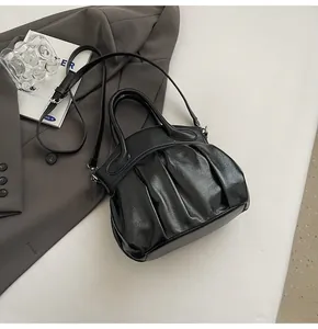 Detail of a black pleated satchel with glossy finish on a grey suit and books
