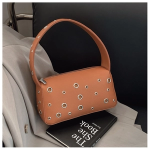 Detail of orange brown underarm bag with silver metal eyelets on textured leather