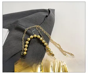 Détail de pochette dorée plissée avec poignée à grosses perles et fine bandoulière chaîne