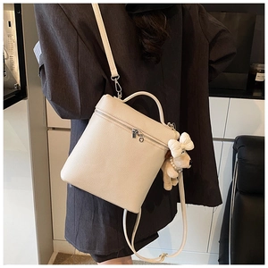 Detail of beige grained leather crossbody bag featuring a cute plush puppy charm