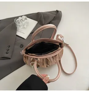 Macro view of metallic pink pleated handbag featuring pearl bow pendant and crossbody strap