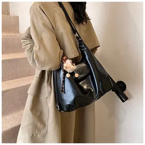 Detail of black glossy faux leather shoulder bag with yellow pom-pom and magnetic buckle