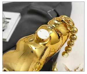 Détail du sac de soirée doré à texture ondulée avec son fermoir rond blanc unique