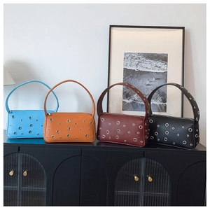 Detail of four colorful rectangle underarm bags with metal eyelets on a black glass table