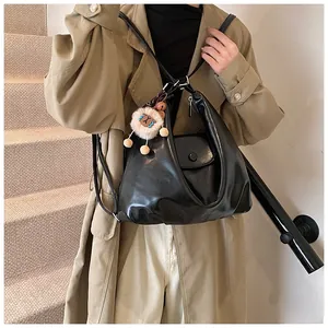 Detail of black glossy hobo bag with plush lion pendant on a beige trench coat