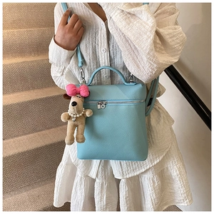 Detail of light blue pebble leather backpack with cute plush puppy charm on model