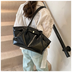 Detail of black glossy tote bag with pleated design and elegant gold buckle hardware