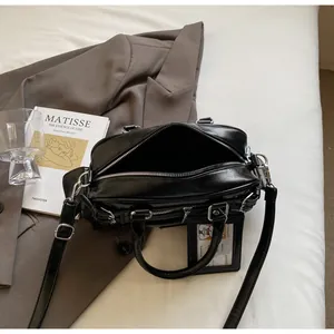 Detail of black glossy PU leather handbag on grey blazer with adjustable strap and charm