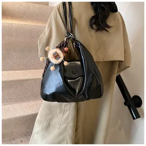 Detail of black glossy leather bag with metal rings, plush pendant and checkered ribbon