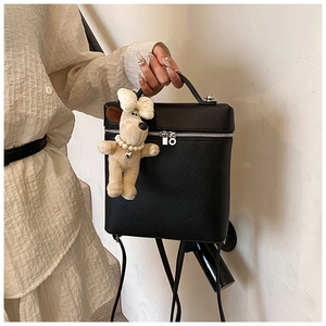 Detail of black pebbled leather backpack featuring silver zippers and cute dog charm