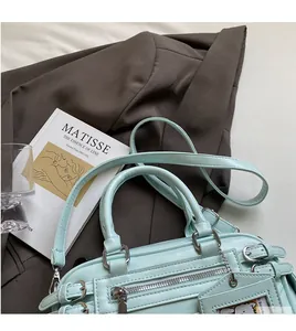Detail of mint green handbag with zippers and straps on a brown blazer and art book