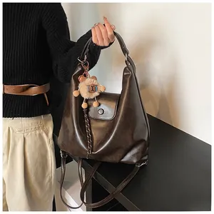 Detail of dark brown vintage oil-wax leather tote bag with cute bear charm and crossbody strap
