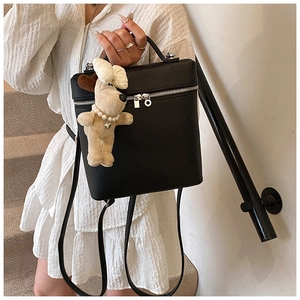 Detail of black lychee grain leather backpack with a cute cream dog plush charm pendant