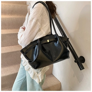 Detailed view of black patent leather tote bag with gold square buckle on a model