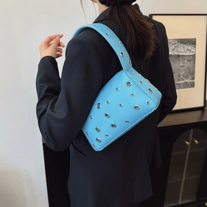 Blue underarm bag with silver eyelet studs and textured leather on a female model