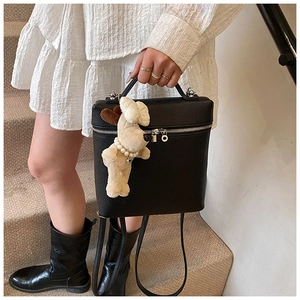 Detail of black lychee grain leather backpack with silver zipper and plush puppy charm